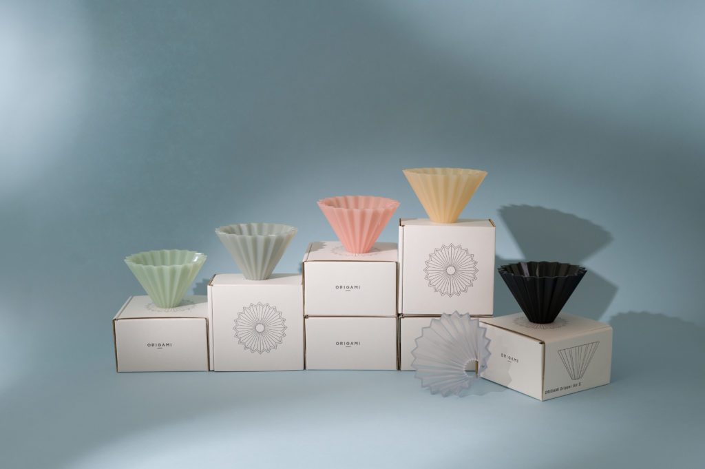 6 multicoloured Origami coffee drippers sitting on white boxes on a baby blue backdrop