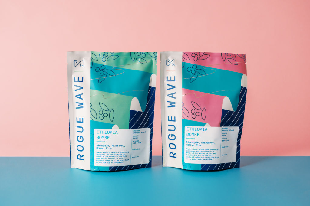1 green and blue Rogue Wave Coffee bag beside 1 pink and blue Rogue Wave Coffee bag sitting on blue and pink background