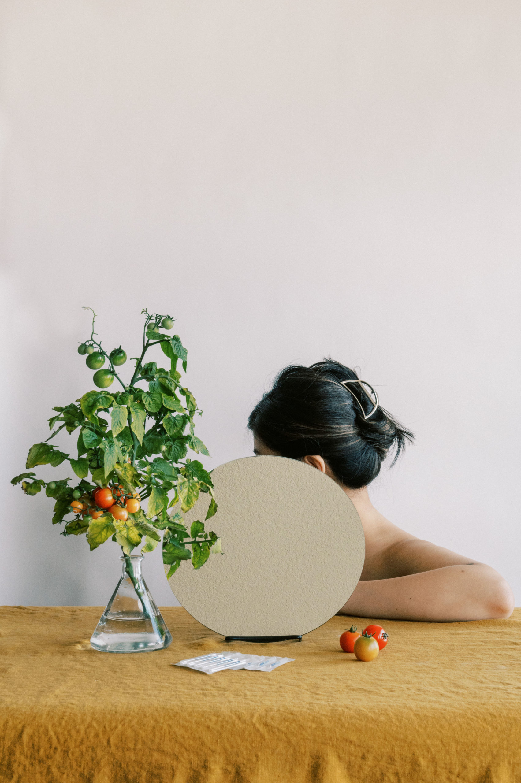 Woman sitting behind mirror with acupuncture tools and tomato plant