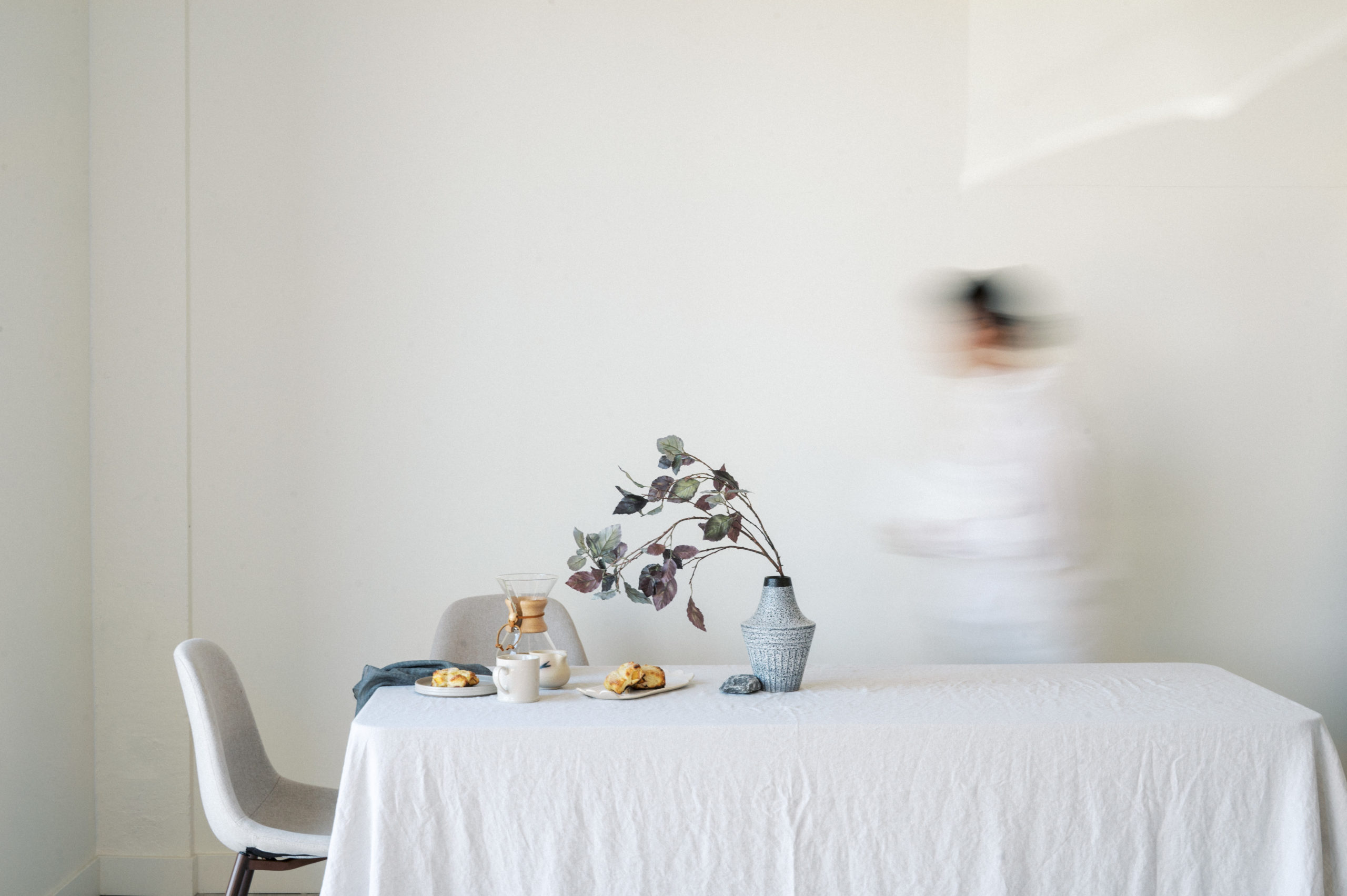 Blurry woman walking behind breakfast table against white wall