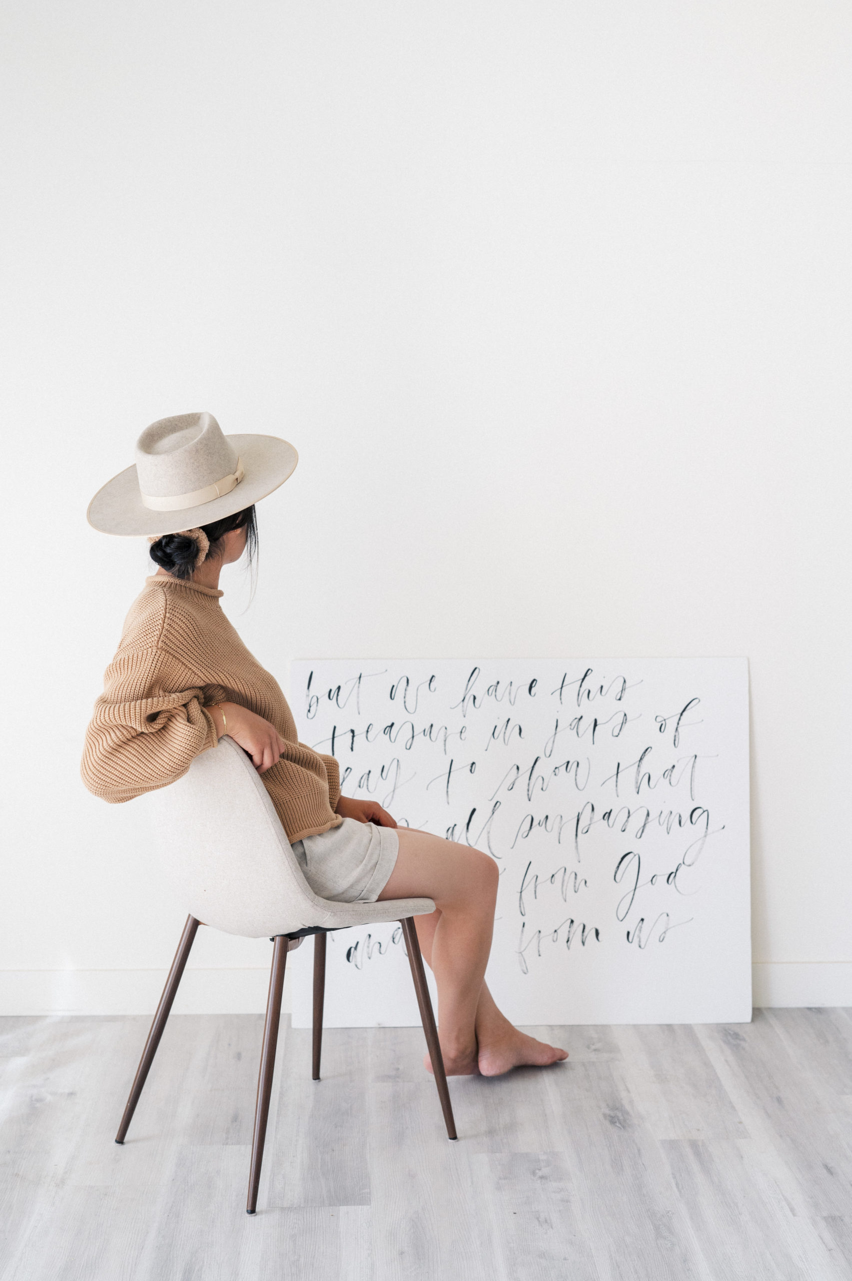 Edmonton Personal Branding Photography  Woman wearing brown sweater sitting in grey chair facing away sitting in front of white board with hand brushed calligraphy