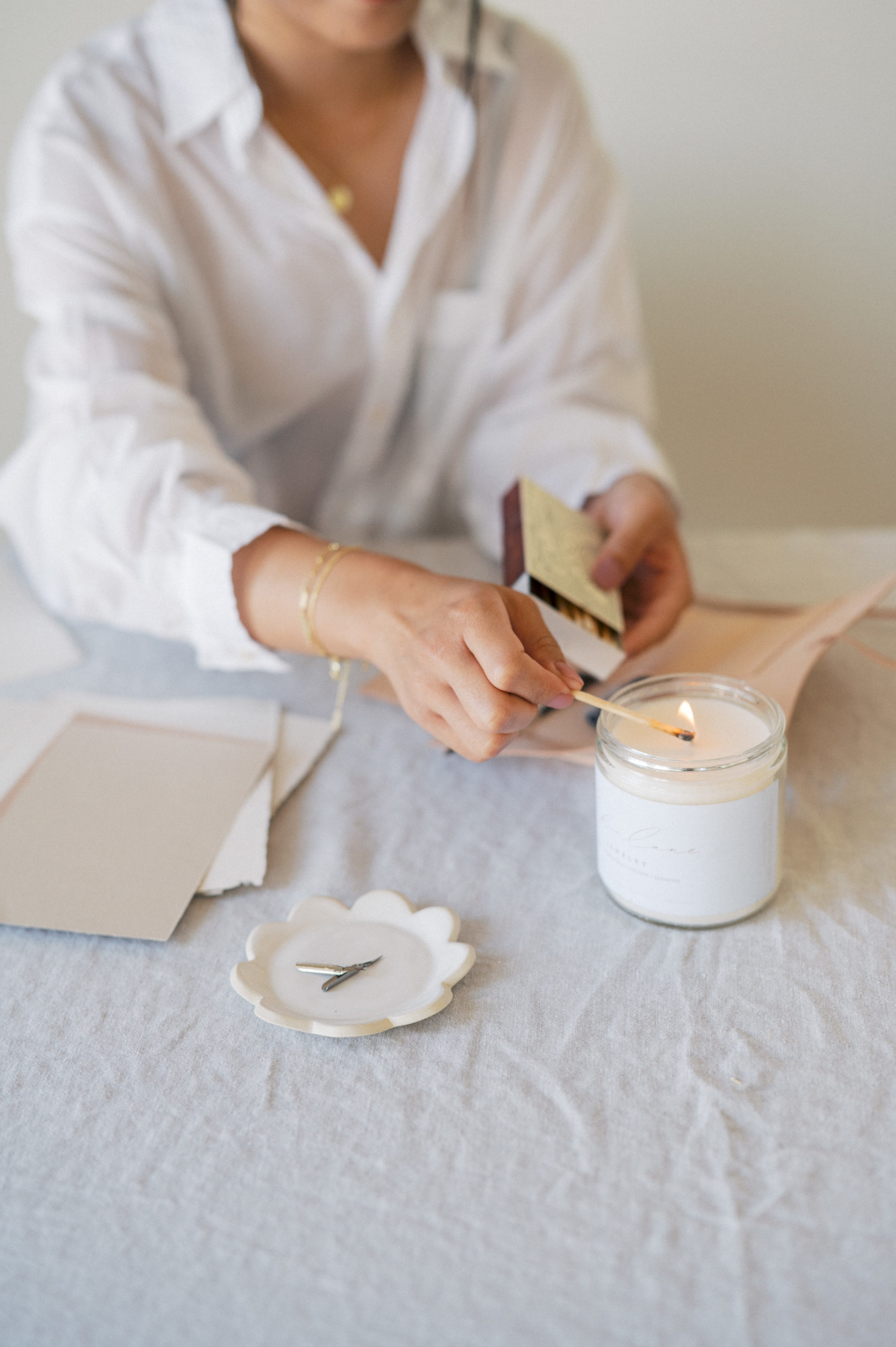 Edmonton Personal Branding Photography  Upclose of woman wearing white button up shirt lighting a white candle on a linen covered table